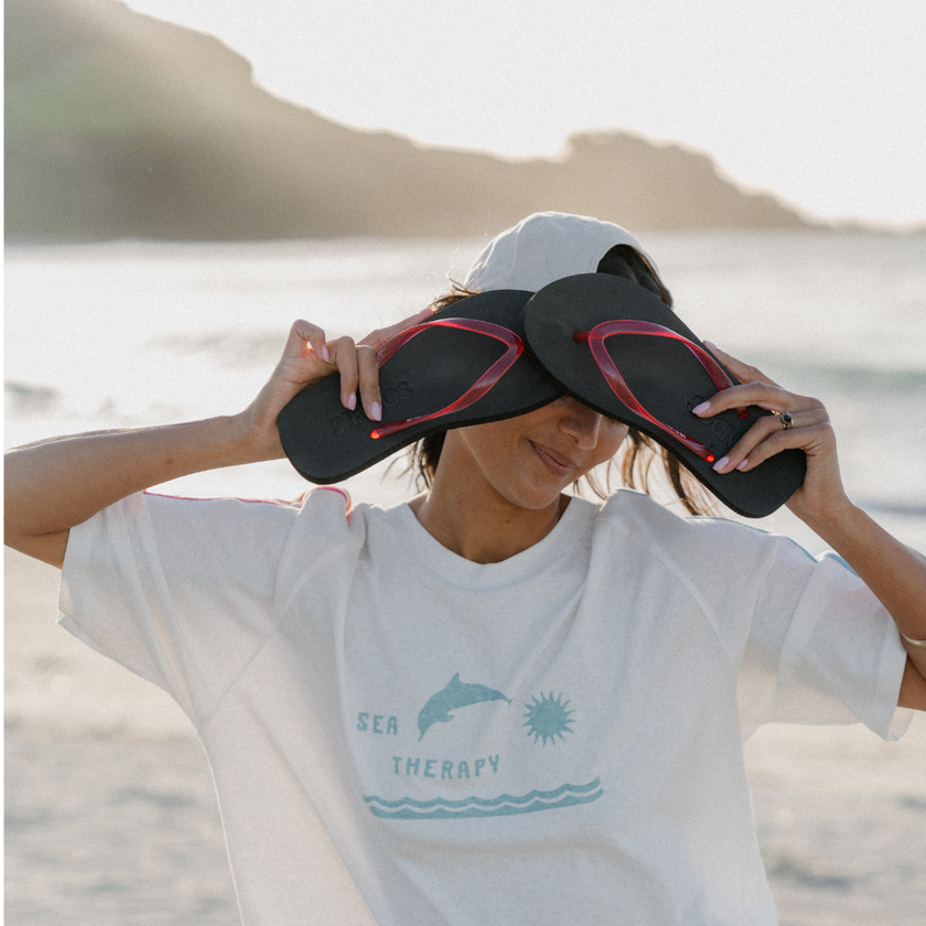 Woman on the beach holding Cherry Bomb Jelly Wide flip flops by Sandos to her head