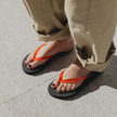 Close-up of Cherry Bomb Jelly Wide flip flops by Sandos, red jelly strap, worn with beige trousers