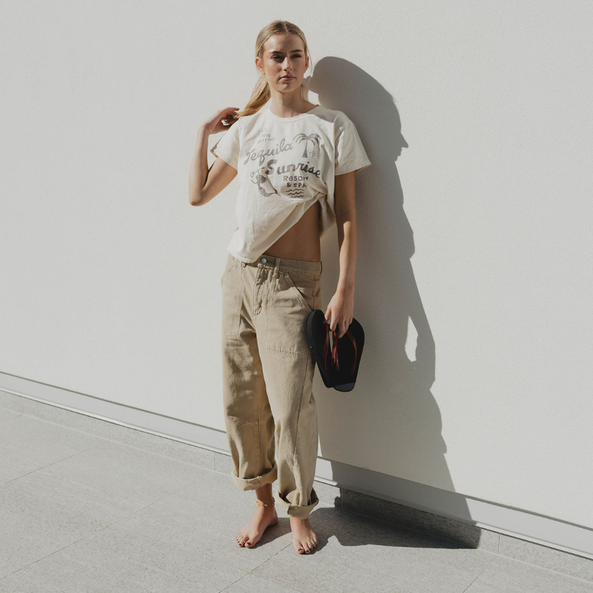 Woman standing against a white wall holding Cherry Bomb Jelly Wide flip flops by Sandos