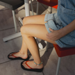 Seated at an outdoor café in denim shorts wearing Cherry Bomb Jelly Wide flip flops by Sandos