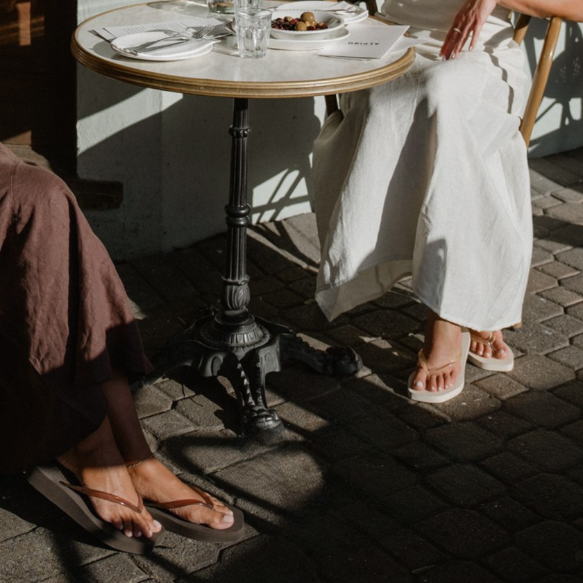 Ecru Jelly Square flip flops by Sandos worn at an outdoor café table