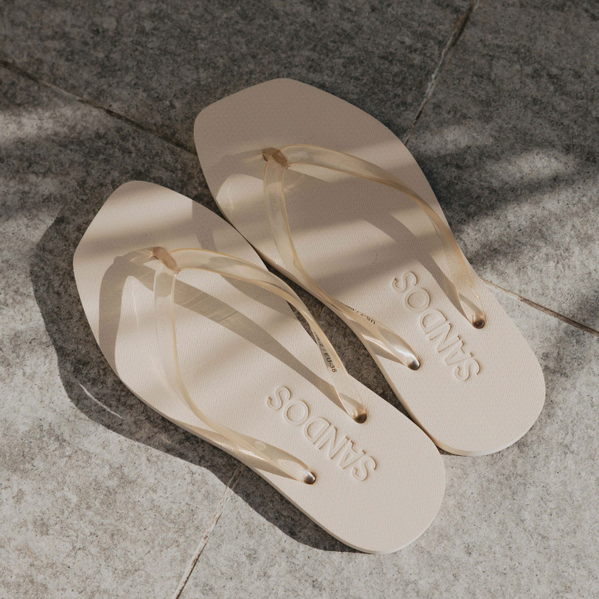 Pair of Ecru Jelly Square flip flops by Sandos on concrete