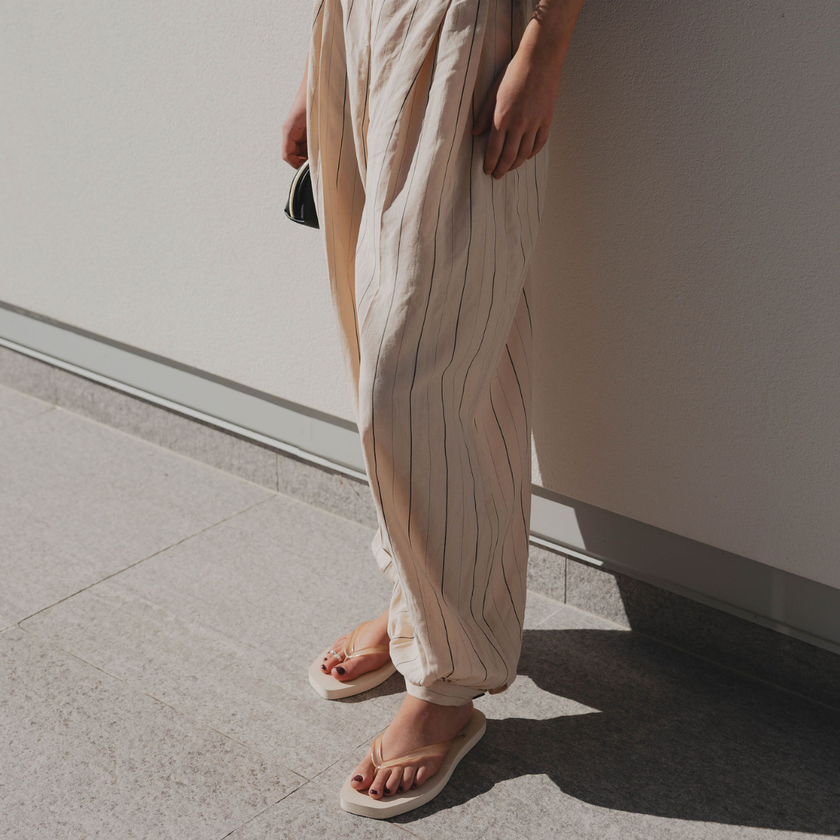 Woman in linen trousers standing in Ecru Jelly Square flip flops by Sandos