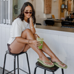 Woman on a stool with an iced matcha wearing Matcha Square flip flops by Sandos