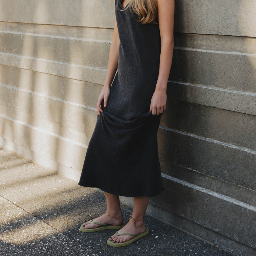 Woman in a black dress standing against a wall wearing Matcha Square flip flops by Sandos