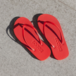 Pair of Red Boyfriend Wide flip flops by Sandos on concrete, top-down view