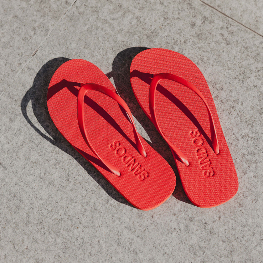 Pair of Red Boyfriend Wide flip flops by Sandos on concrete, top-down view