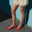 Woman by a teal wall wearing Red Boyfriend Wide flip flops by Sandos