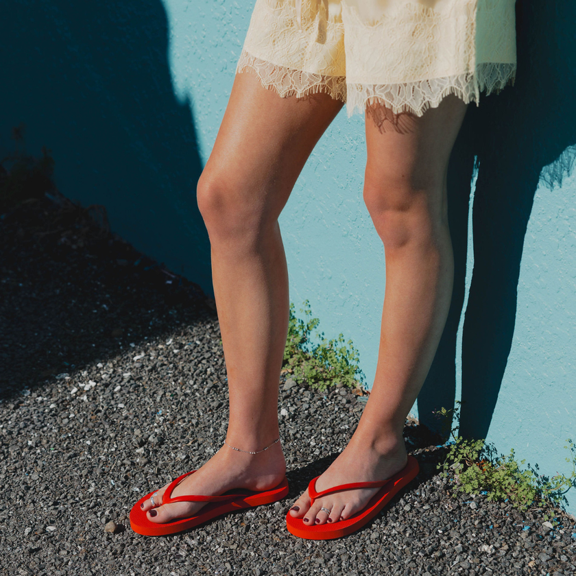 Woman by a teal wall wearing Red Boyfriend Wide flip flops by Sandos
