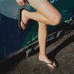 Woman leaning against a teal wall wearing Truffle Boyfriend Wide flip flops by Sandos