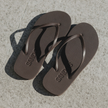 Pair of dark brown Truffle Boyfriend Wide flip flops by Sandos on concrete