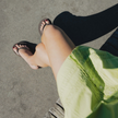 Looking down at Truffle Boyfriend Wide flip flops by Sandos with a green skirt